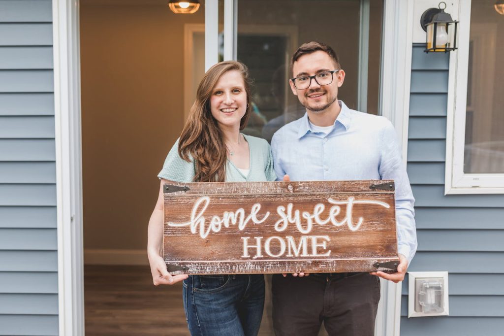 Couple Holding a Wooden Home Sweet Home Sign in hope for meeting your neighbors after moving