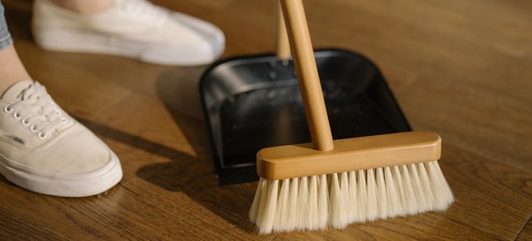 Person Wearing White Pants and White Socks Standing Beside Brown Broom